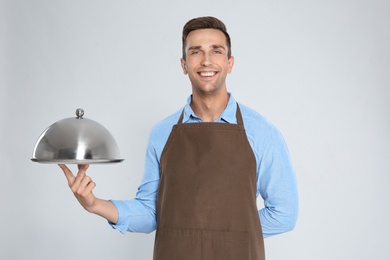 Photo of Handsome waiter holding metal tray with lid on light background