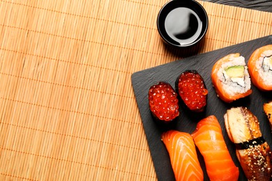 Photo of Delicious sushi rolls and soy sauce on mat, flat lay. Space for text