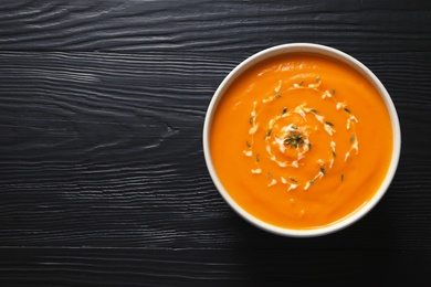 Delicious pumpkin cream soup in bowl on wooden background, top view. Space for text