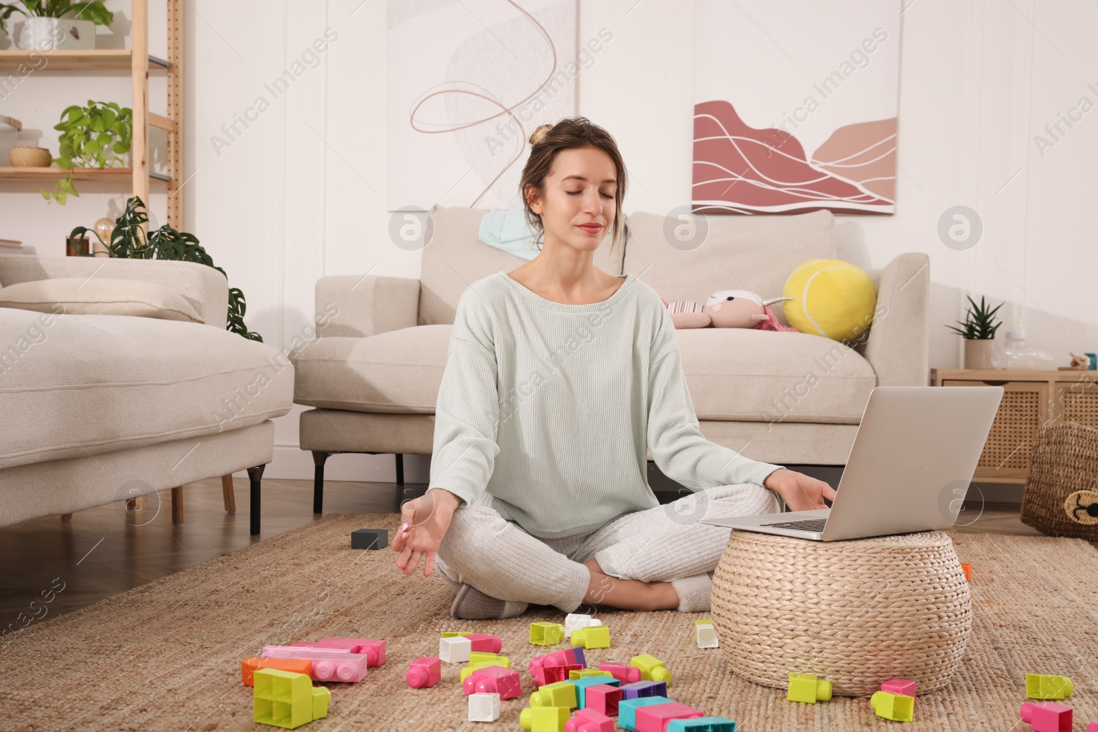 Photo of Young mother meditating on floor in messy living room