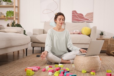 Young mother meditating on floor in messy living room