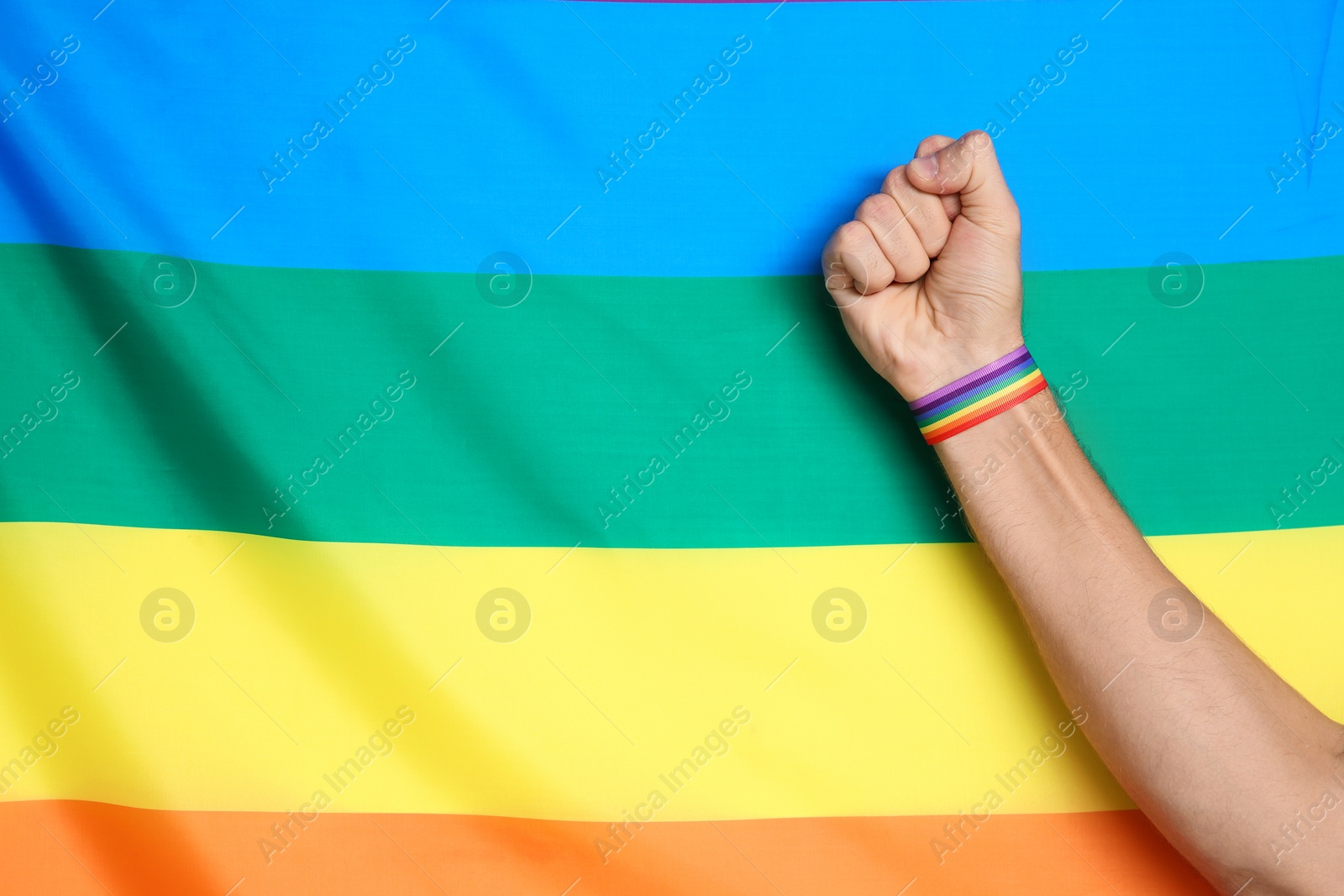 Photo of Man wearing gay wristband on hand near rainbow flag, closeup. Space for text