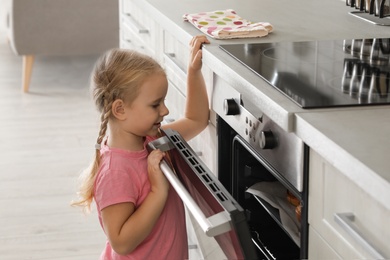 Photo of Little girl opening oven while baking in kitchen