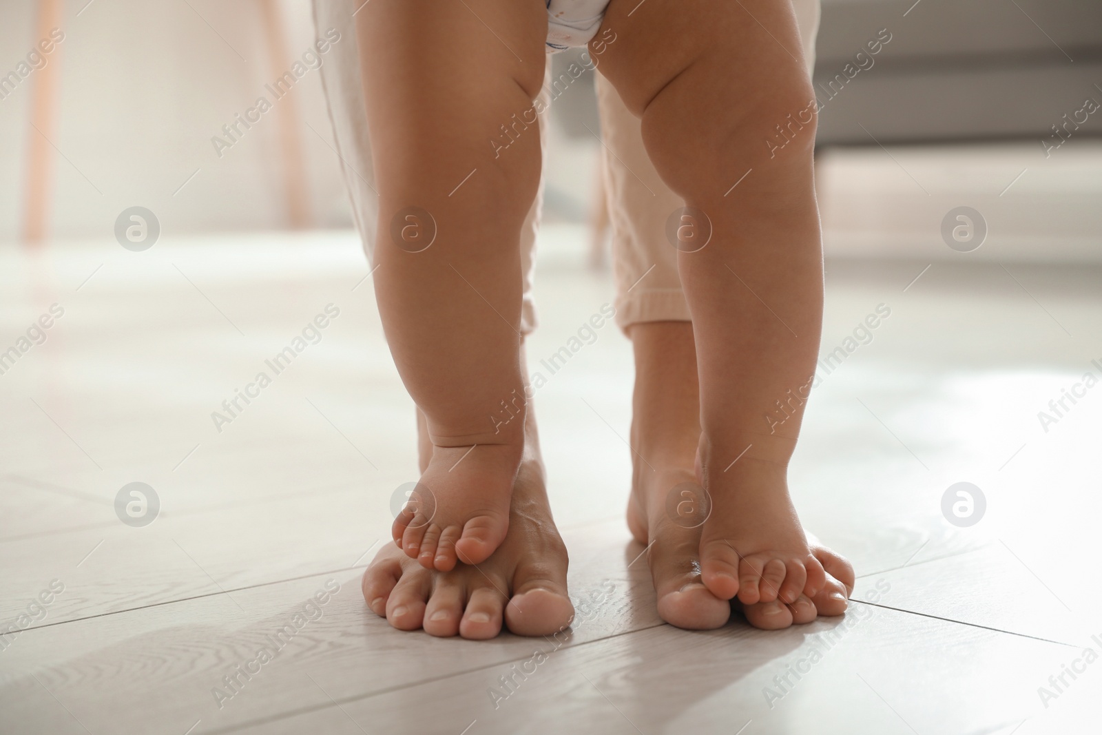 Photo of Mother supporting her baby daughter while she learning to walk at home, closeup