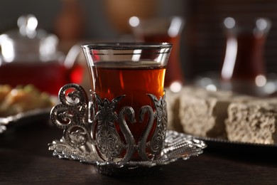 Photo of Glass of traditional Turkish tea in vintage holder on wooden table, closeup