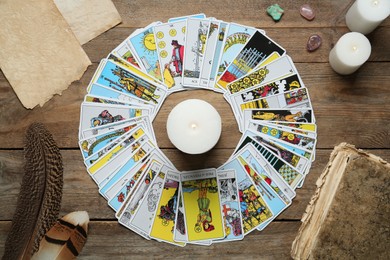 Burning candle surrounded by tarot cards on wooden table, flat lay