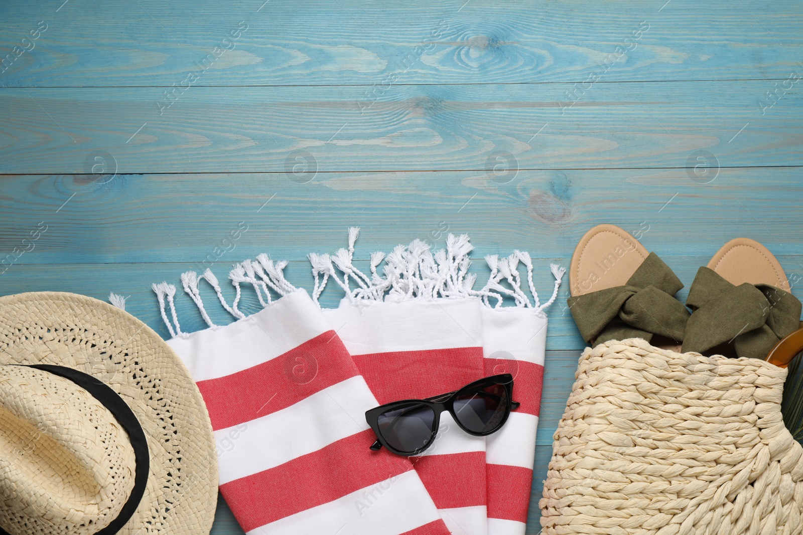 Photo of Beach towel, sunglasses, hat and straw bag with slippers on light blue wooden background, flat lay. Space for text