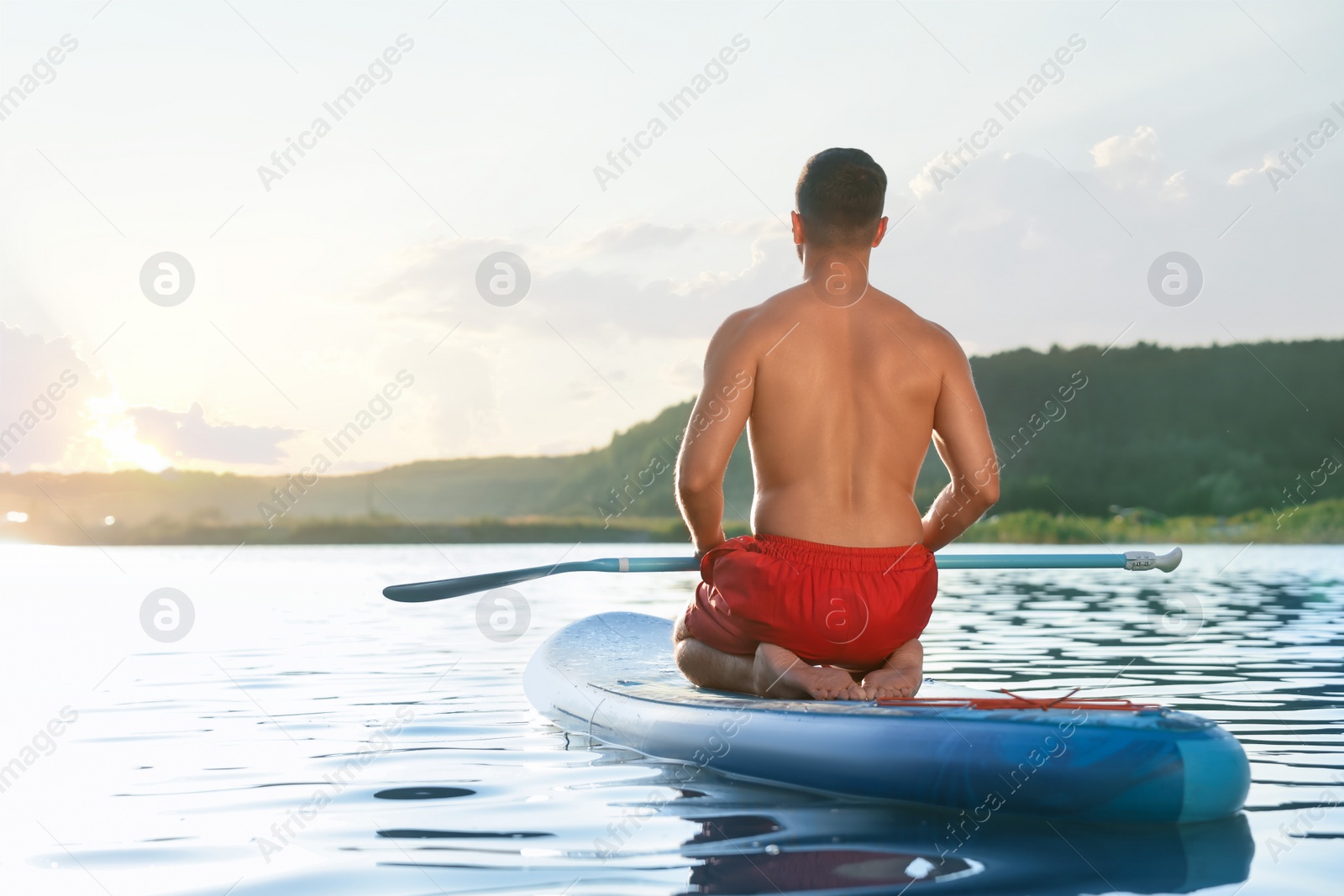 Photo of Man paddle boarding on SUP board in river at sunset, back view