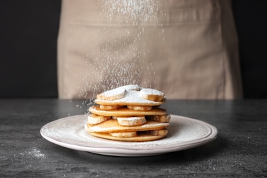 Sprinkling of delicious pancakes with powdered sugar on table