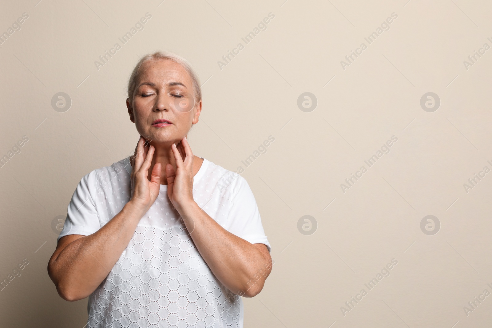 Photo of Mature woman doing thyroid self examination on beige background, space for text