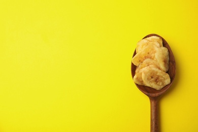 Photo of Wooden spoon with banana slices on color background, top view with space for text. Dried fruit as healthy snack