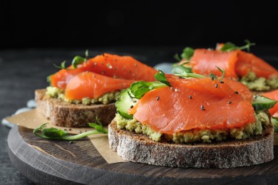 Photo of Tasty bruschettas with salmon, guacamole and microgreens on table, closeup