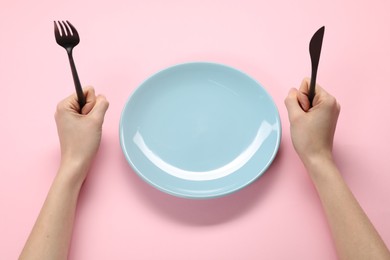 Photo of Woman with fork, knife and empty plate at pink table, closeup