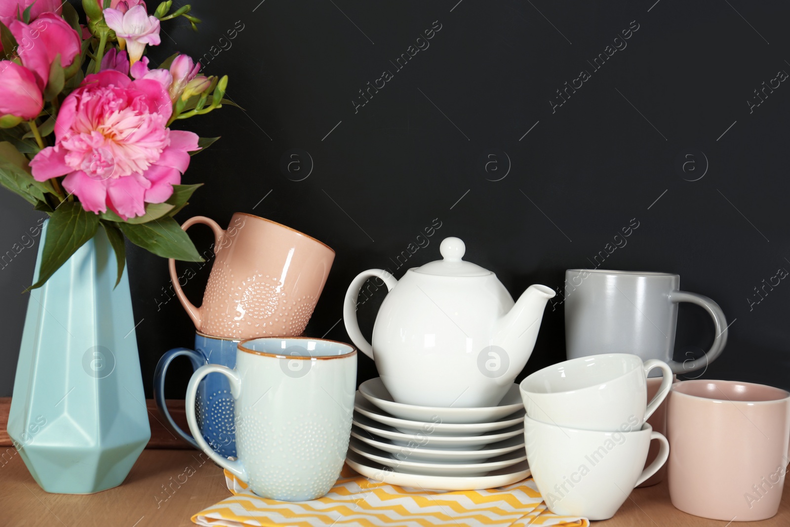 Photo of Set of dishware and vase with flowers on table near chalkboard