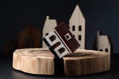 Photo of House model in cracked wooden stump on black table depicting earthquake disaster