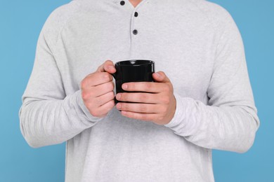 Man holding black mug on light blue background, closeup