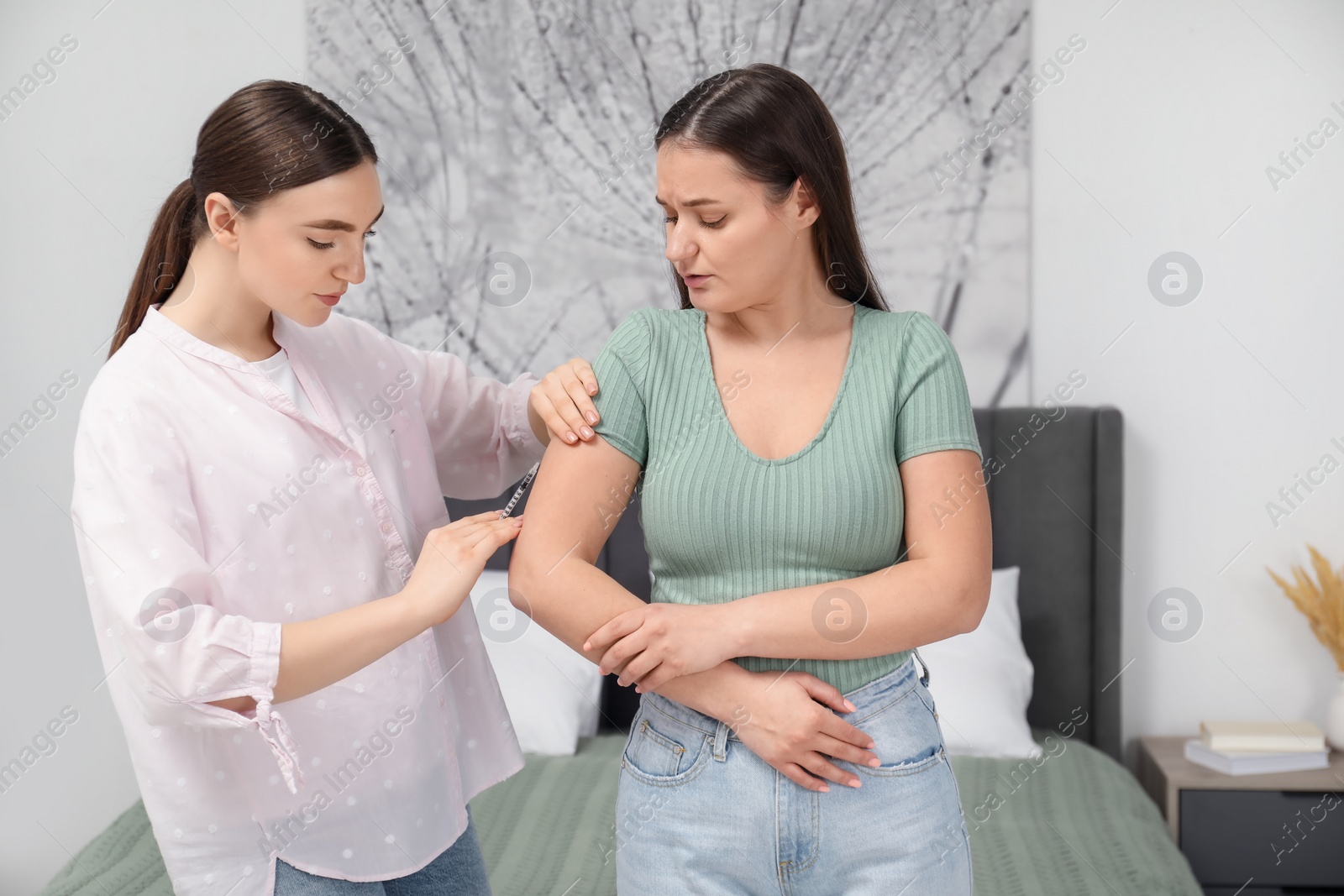 Photo of Woman giving insulin injection to her diabetic friend in bedroom