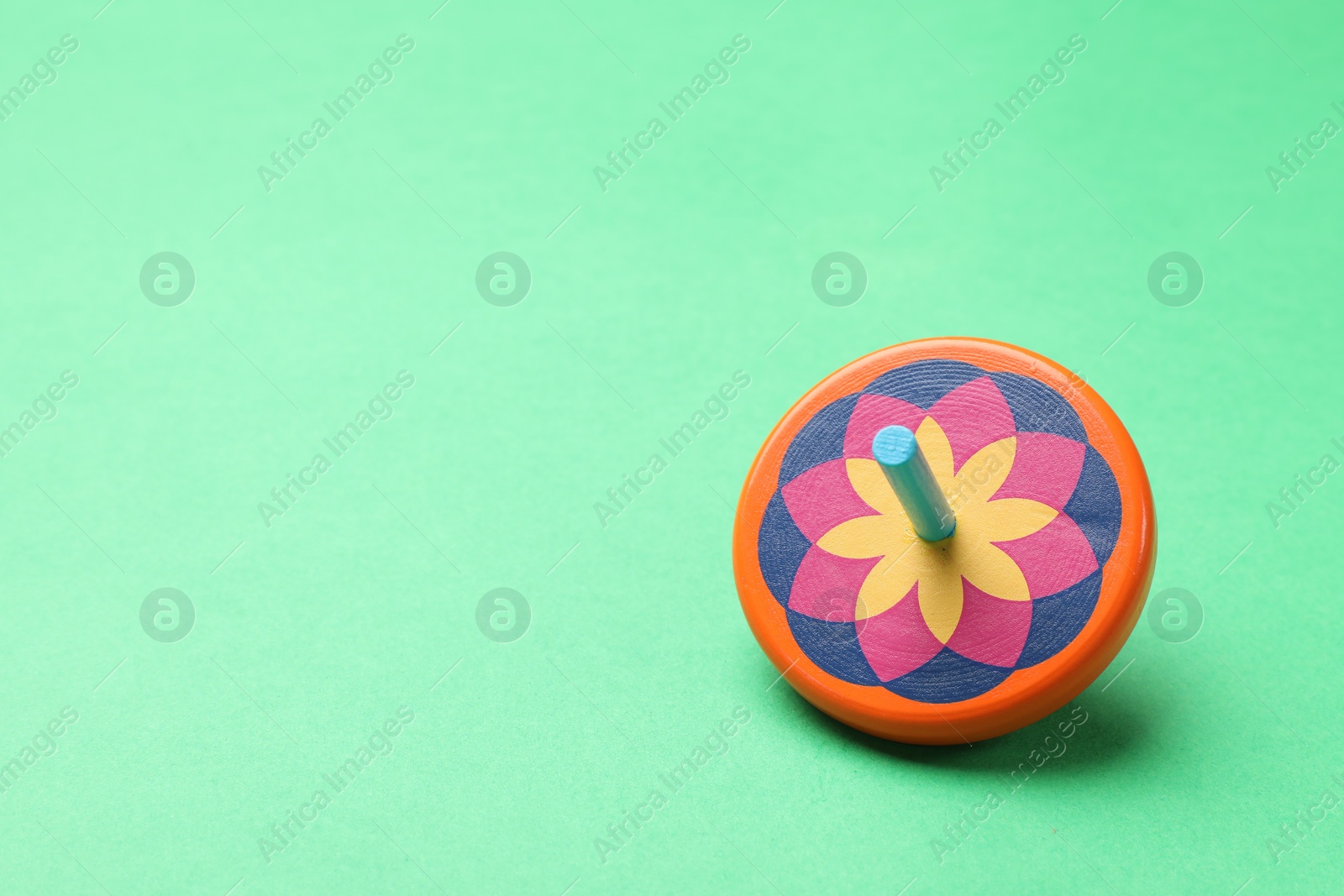 Photo of One colorful spinning top on green background, space for text