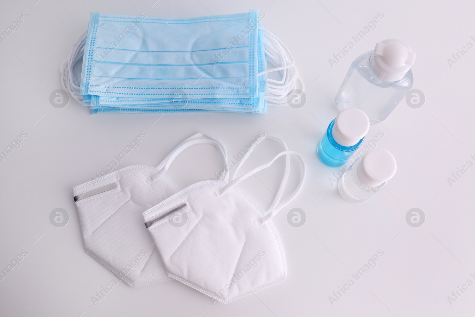 Photo of Hand sanitizers and respiratory masks on white background, flat lay. Protective essentials during COVID-19 pandemic