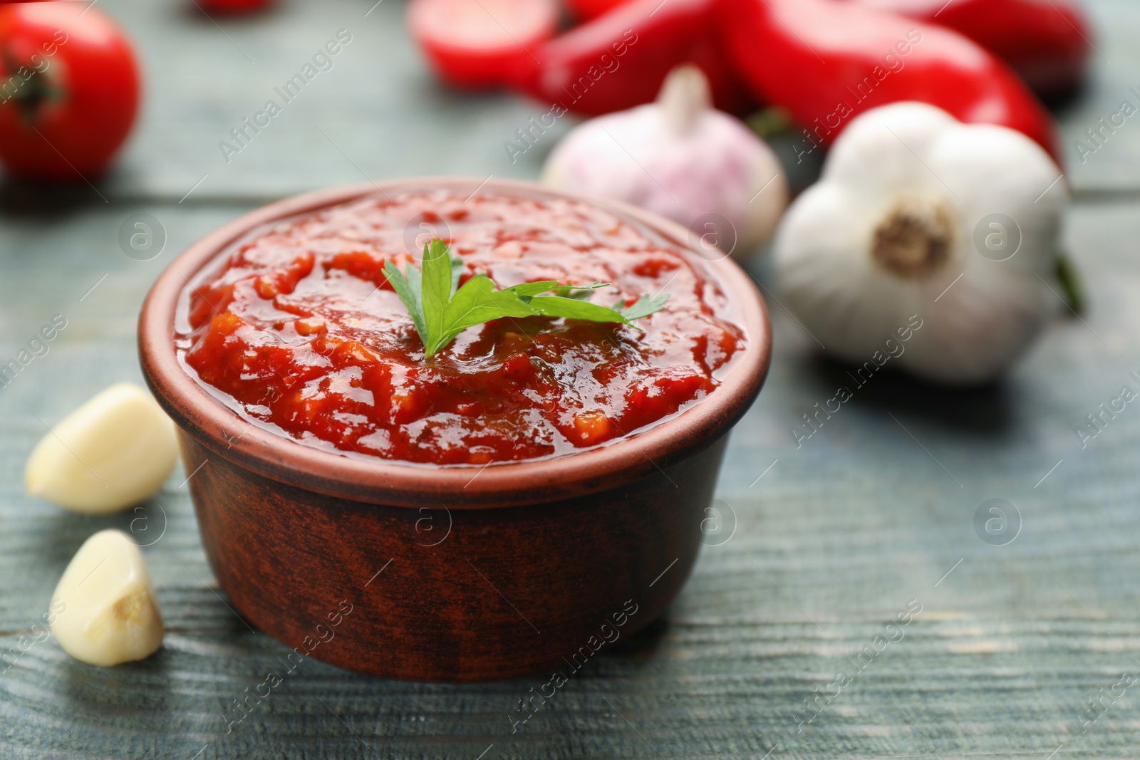 Photo of Delicious adjika sauce in bowl and ingredients on light blue wooden table, closeup