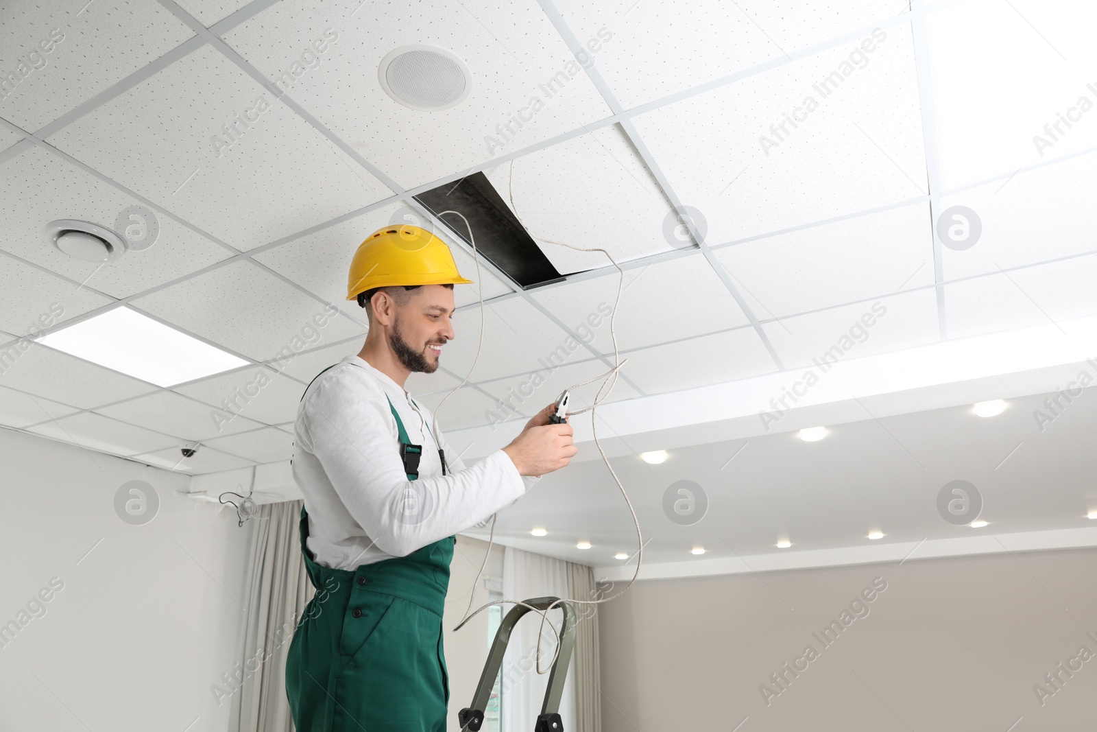 Photo of Electrician with pliers repairing ceiling wiring indoors