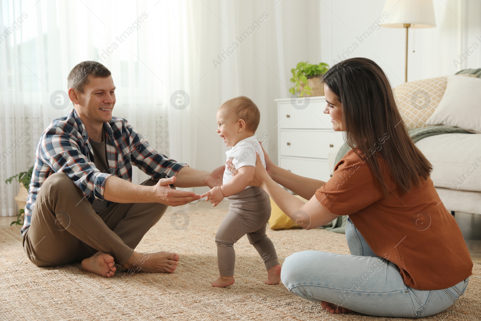 Photo of Parents supporting their baby daughter while she learning to walk at home