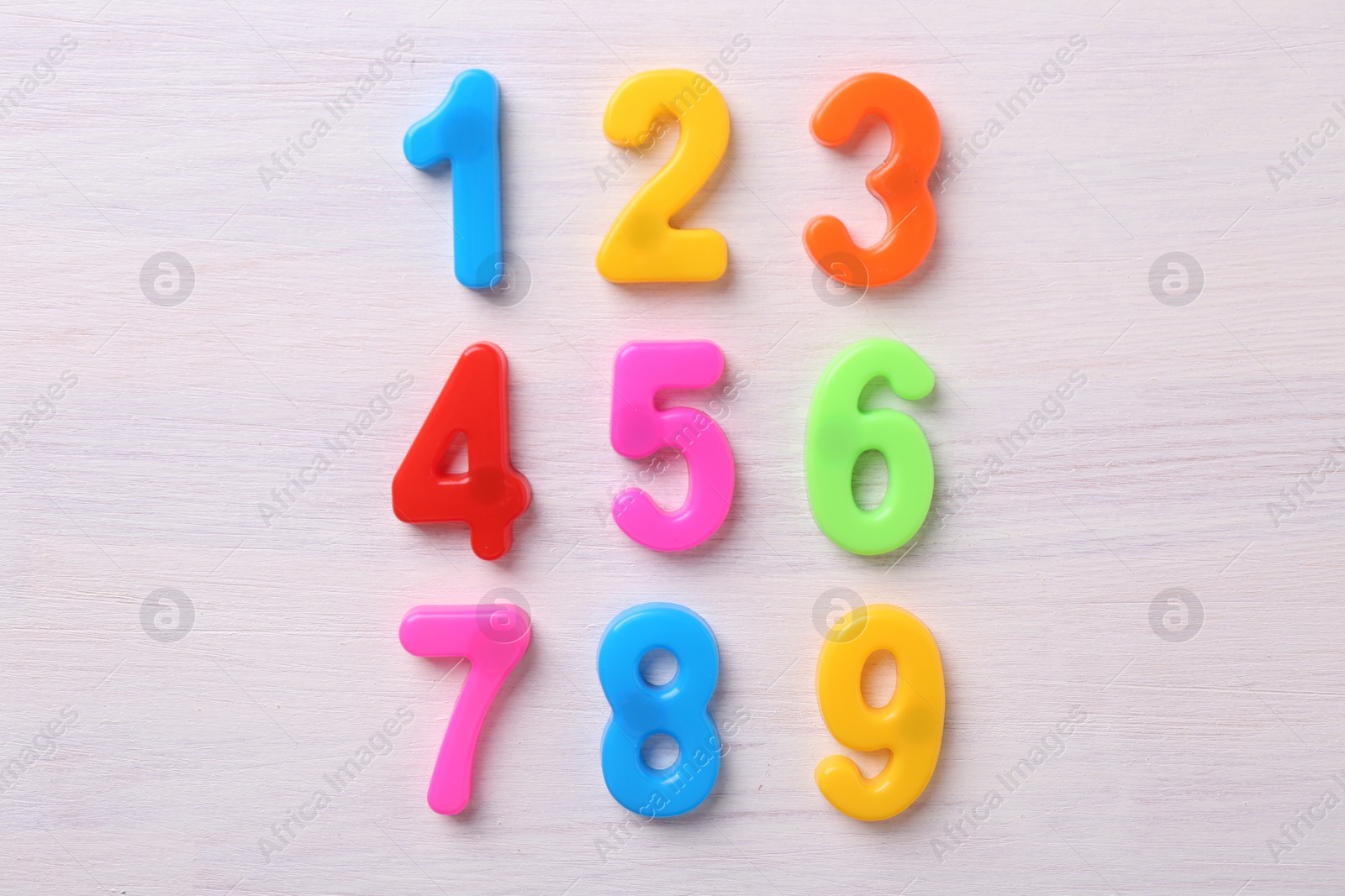 Photo of Colorful numbers on white wooden school desk, flat lay