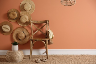 Wooden chair with bag and straw hats on brown wall, space for text. Interior design