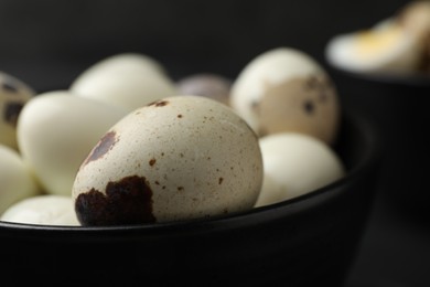 Unpeeled and peeled boiled quail eggs in bowl on black table, closeup