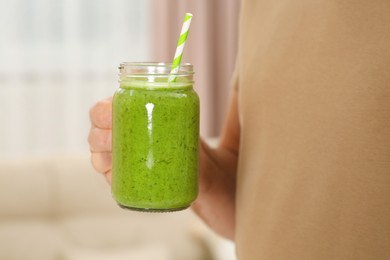 Man holding mason jar with delicious smoothie indoors, closeup