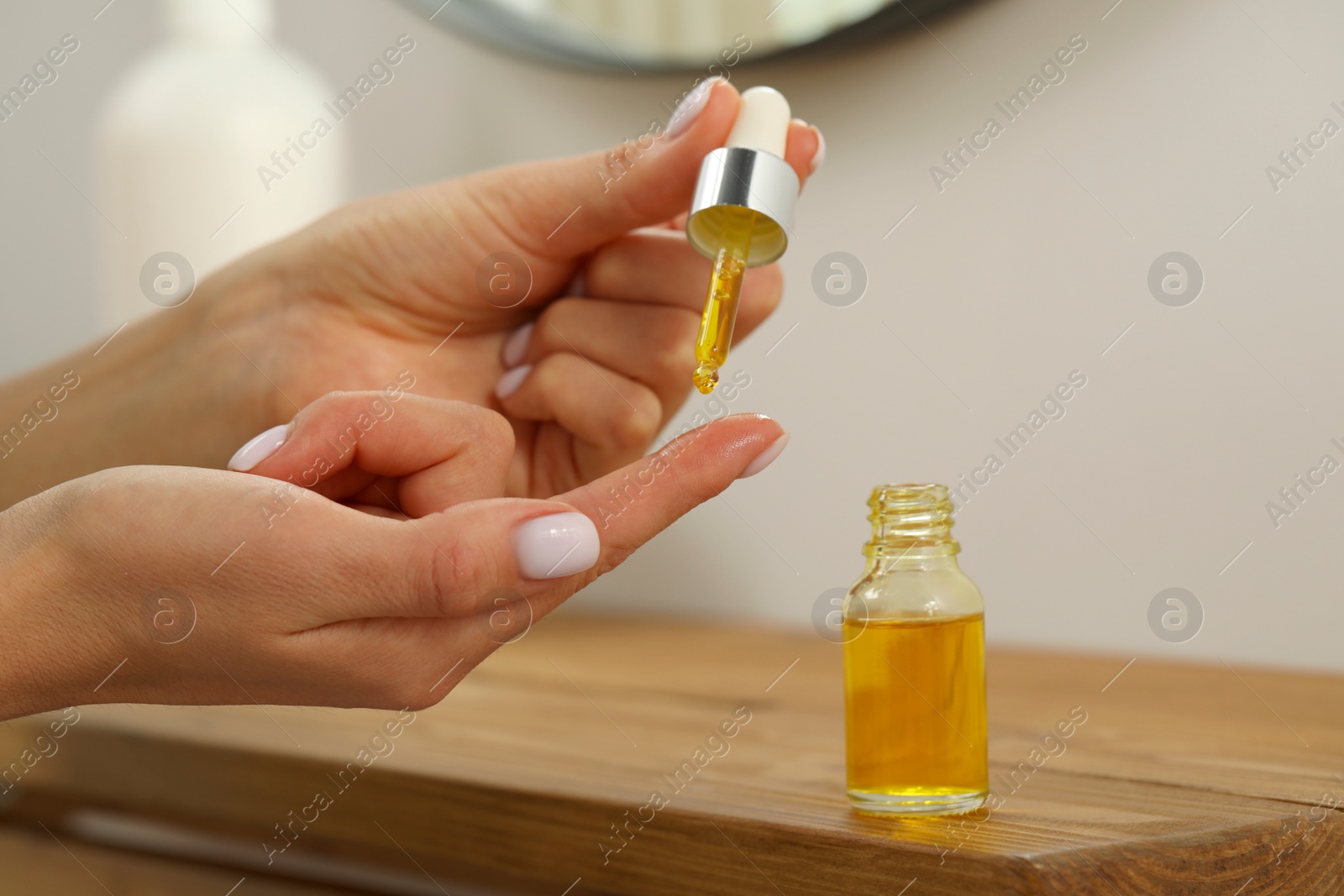 Photo of Young woman dripping essential oil on finger indoors, closeup
