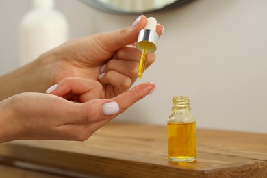 Photo of Young woman dripping essential oil on finger indoors, closeup