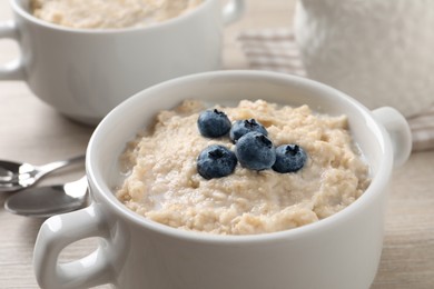 Photo of Tasty oatmeal porridge with blueberries in bowl on light table, closeup