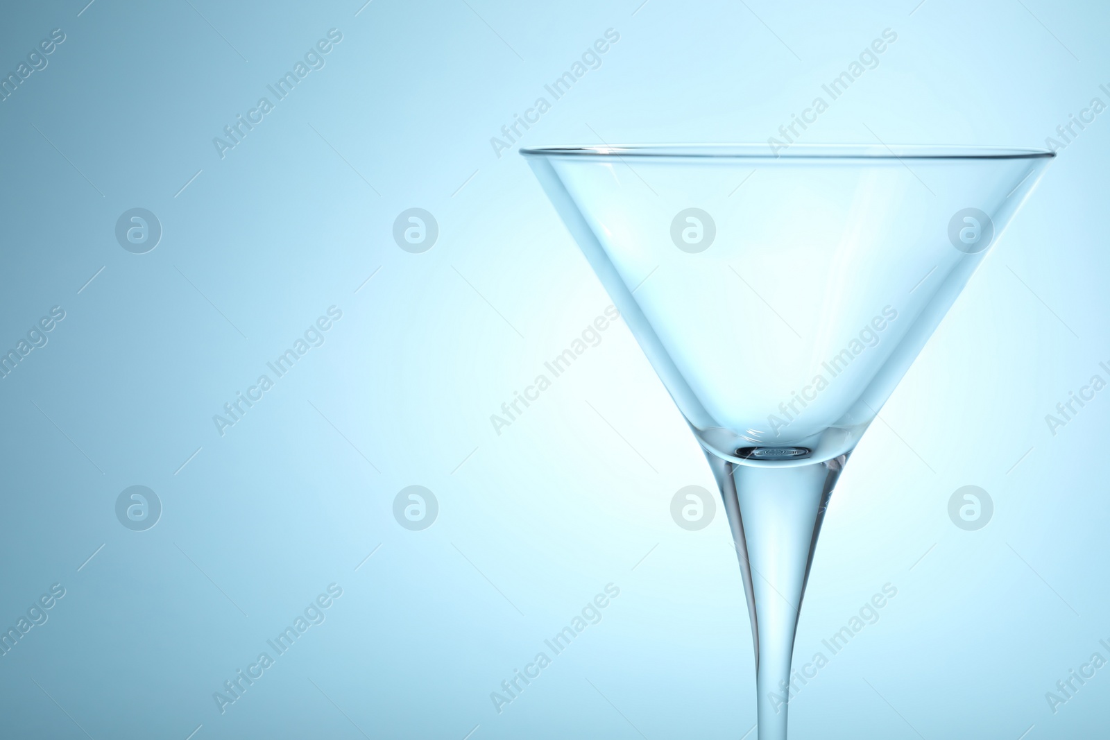 Photo of Elegant empty martini glass on light blue background, closeup. Space for text