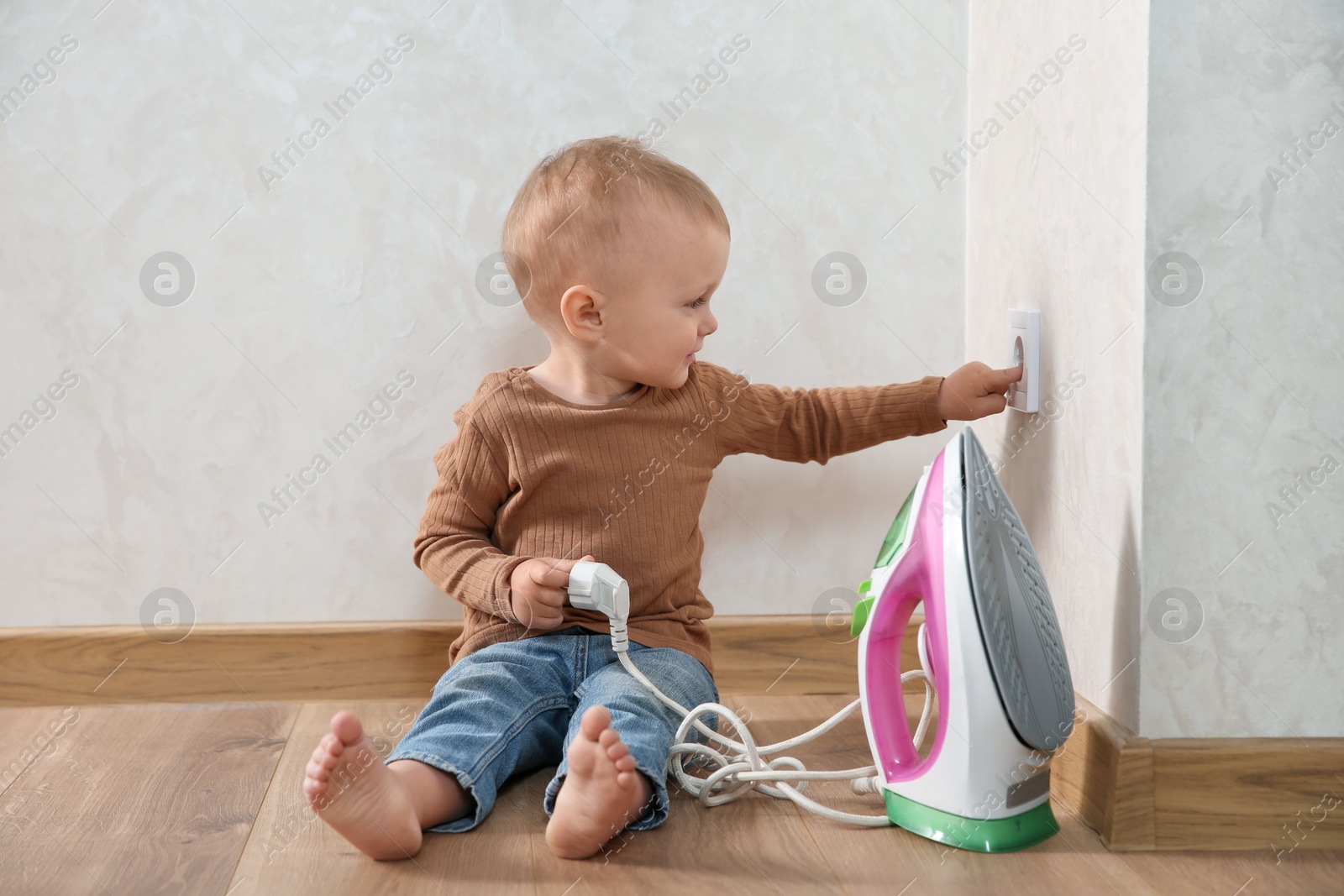 Photo of Little child playing with electrical socket and iron plug at home. Dangerous situation