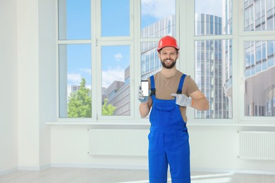 Photo of Professional repairman in uniform with phone indoors, space for text