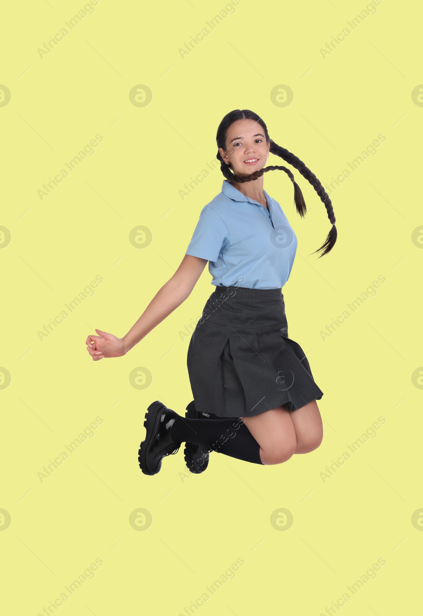 Image of Happy cute girl in school uniform jumping on light yellow background