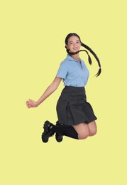 Image of Happy cute girl in school uniform jumping on light yellow background