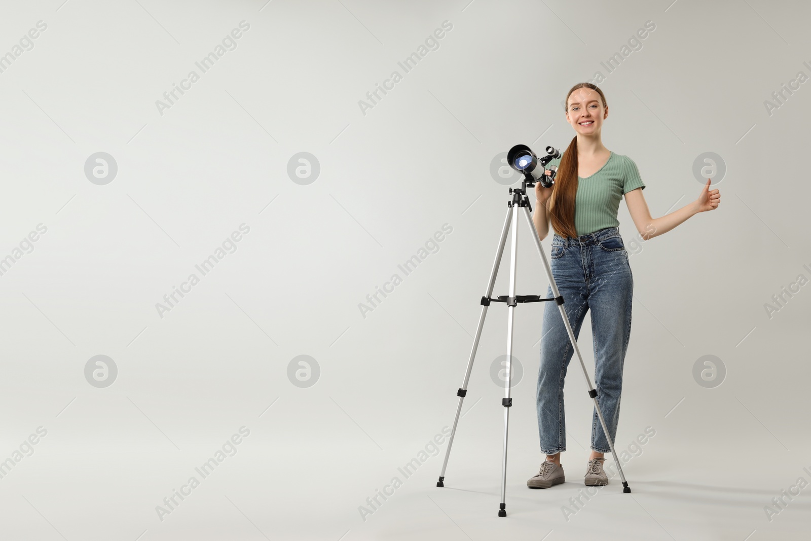 Photo of Happy astronomer with telescope showing thumbs up on grey background, space for text