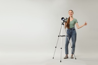 Happy astronomer with telescope showing thumbs up on grey background, space for text