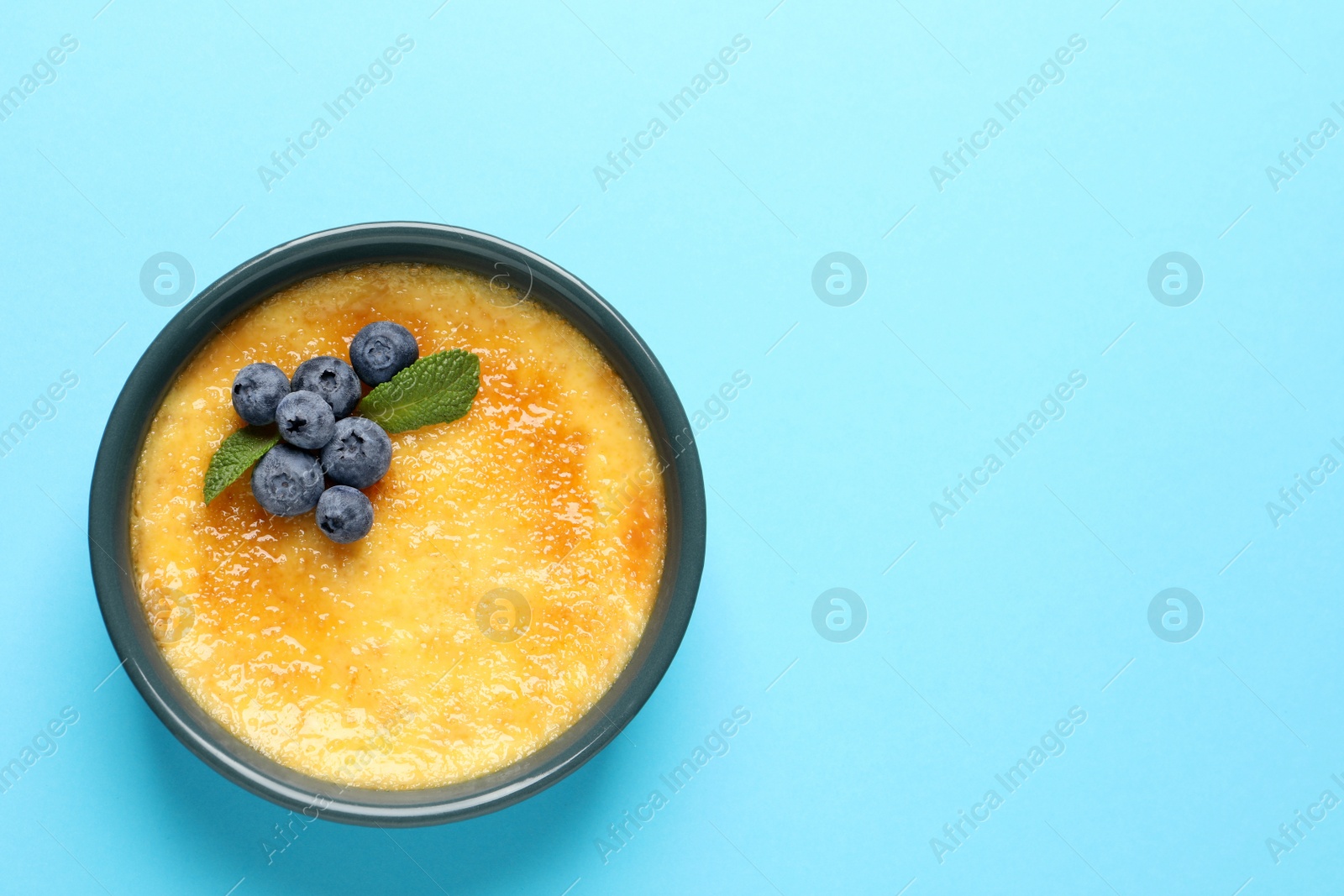 Photo of Delicious creme brulee with fresh blueberries and mint on light blue background, top view. Space for text