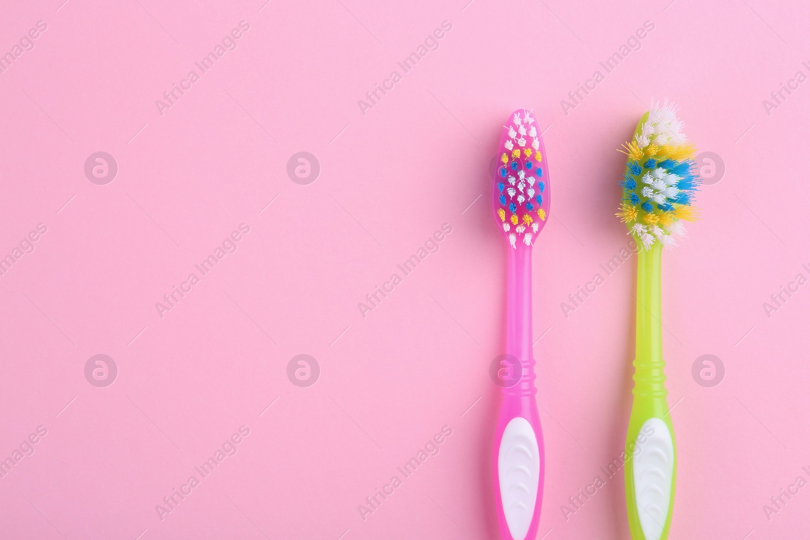 Photo of Colorful plastic toothbrushes on pink background, flat lay. Space for text