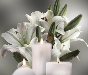 Image of Funeral. Beautiful lilies and burning candles on light grey background, bokeh effect