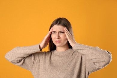 Photo of Young woman suffering from migraine on yellow background