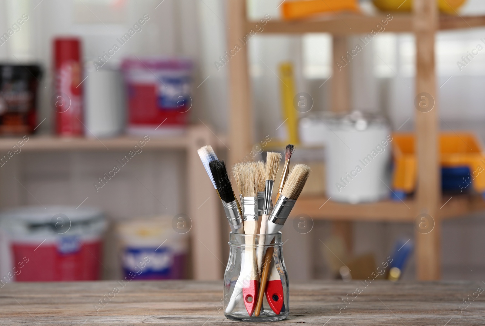 Photo of Glass jar with paint brushes on wooden table in workshop. Space for text
