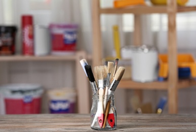 Glass jar with paint brushes on wooden table in workshop. Space for text