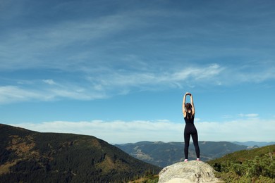 Photo of Beautiful young woman stretching on rock in mountains, back view