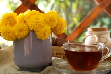 Photo of Beautiful yellow chrysanthemum flowers and cup of aromatic tea on table