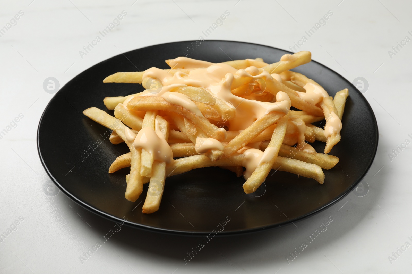 Photo of Delicious French fries with cheese sauce on white table, closeup