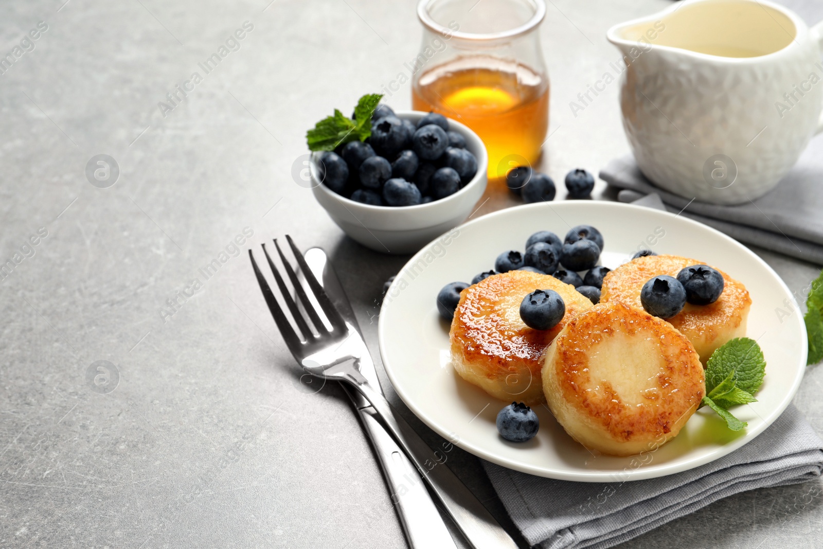 Photo of Delicious cottage cheese pancakes with blueberries, mint and honey on light grey table, space for text